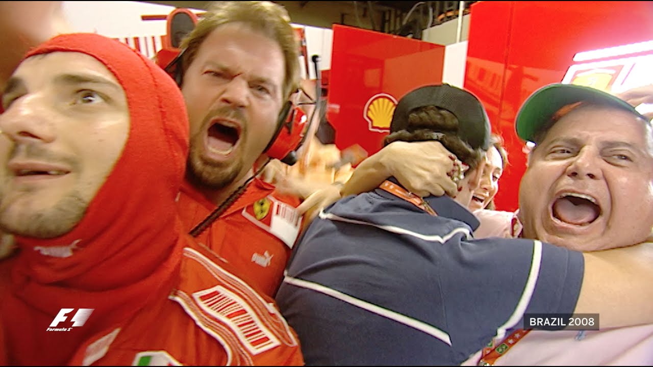 The Ferrari mechanics cheer with mouths open. The team is wearing red Ferrari outfits with a red Ferrari background behind