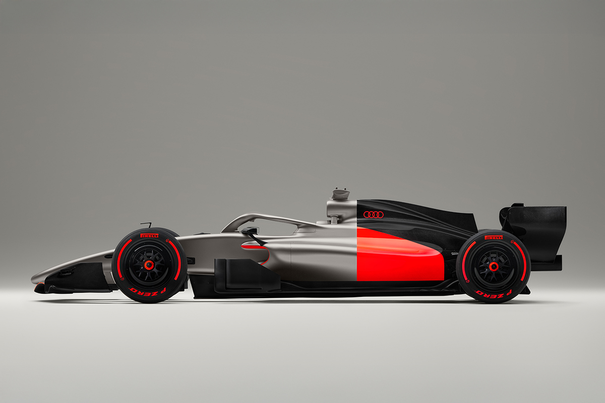 A side profile of the Audi R26 Concept car, Audi's livery unveiling ahead of their F1 debut in 2026. The car features a sleek design in metallic silver, black, and red accents, with Pirelli tires and a minimal background.